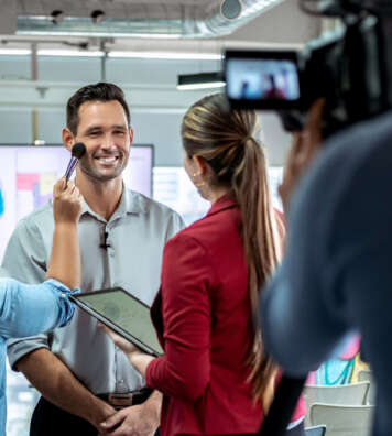 Happy businessman during corporate interview with journalist. Vip or manager talking and smiling in office. Woman at work as makeup artist with business man and cameraman shooting video with camera