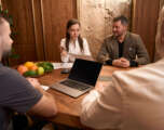 Woman showing prescription to male at table Young female nurse sitting at desk with doctors next to smiling man and holding papers